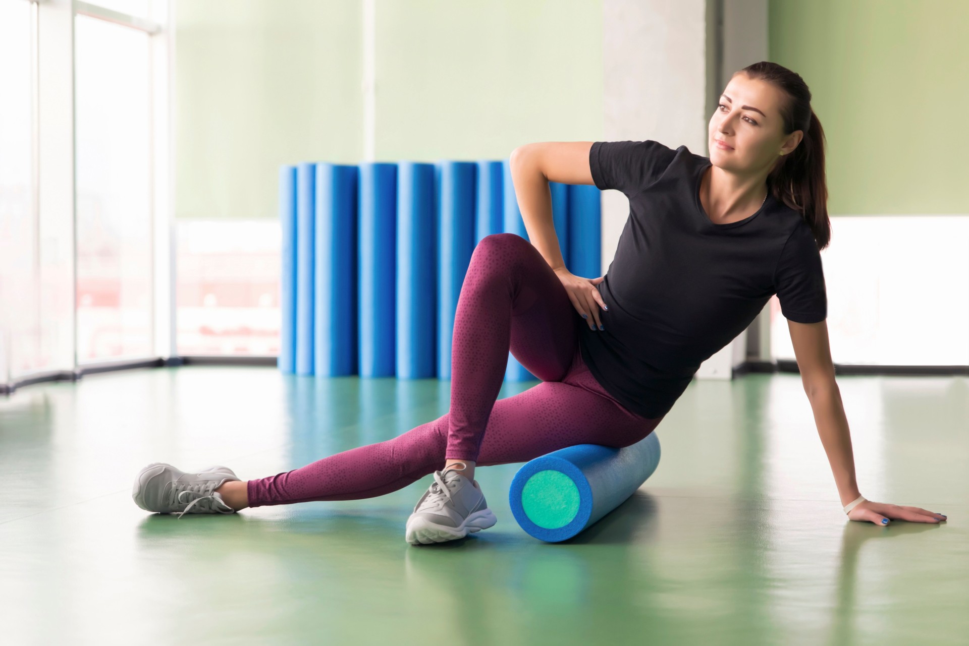 Attractive female doing foam roller exercise and posing in modern bright fitness center